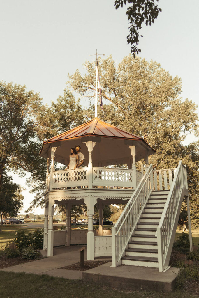 Engaged couple looks off of gazebo during White Bear Lake golden hour.