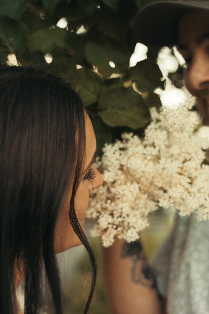 Woman smells hydrangeas as her husband looks on with a smile on his face. 