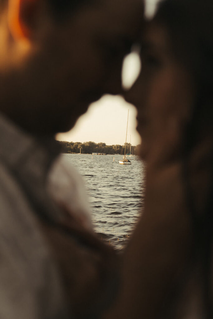 Couple rests their foreheads against each other as sailboats are off in the distance. 