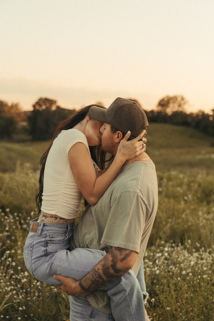 Man picks up his fiance to kiss her as she wraps her legs around him.