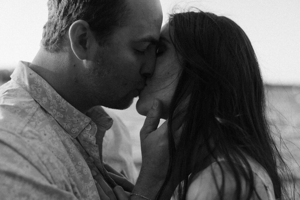 Engaged couple kisses alongside lake in Minnesota. 