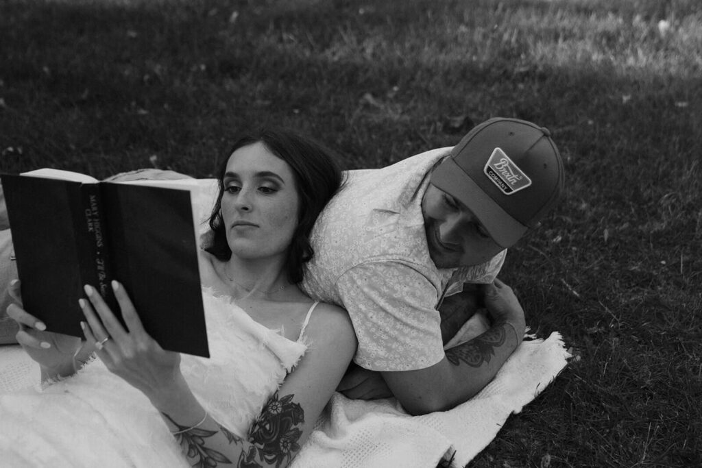 Engaged couple reads book in the grass.