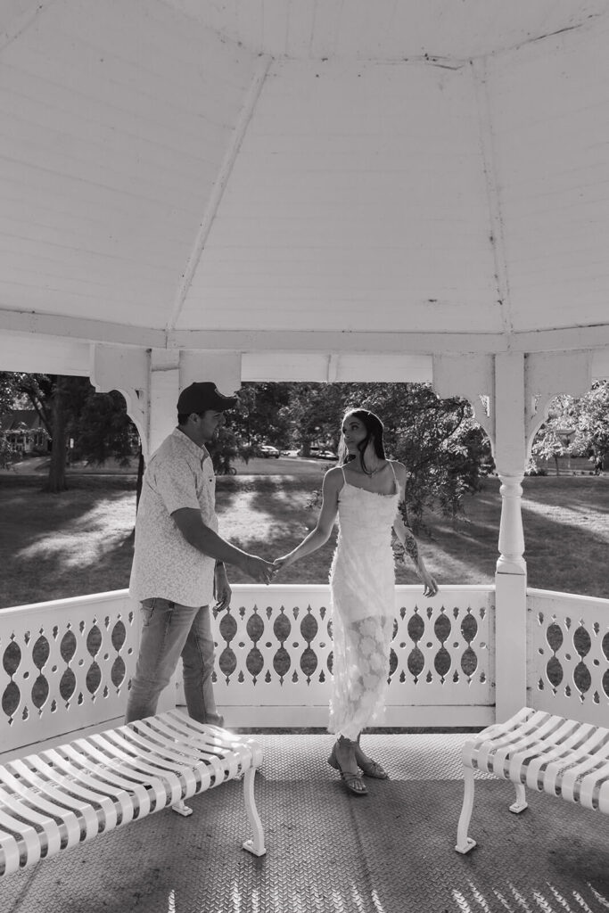 Man and woman walk hand in hand through gazebo.