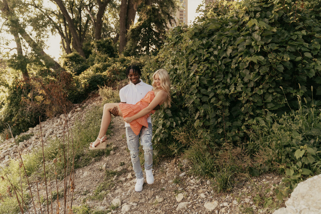 Senior photos Minneapolis with high school boy carrying his girlfriend across the rocks by the creek