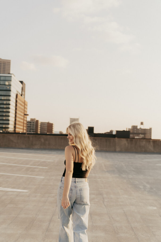 High school senior wearing light wash denim jeans and black tank top walks on parking ramp in downtown Minneapolis