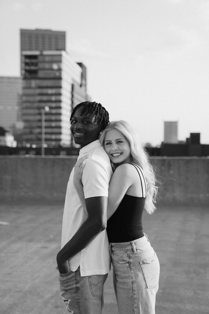 Girl hugs her boyfriend from behind while posing on rooftop parking ramp in downtown Minneapolis