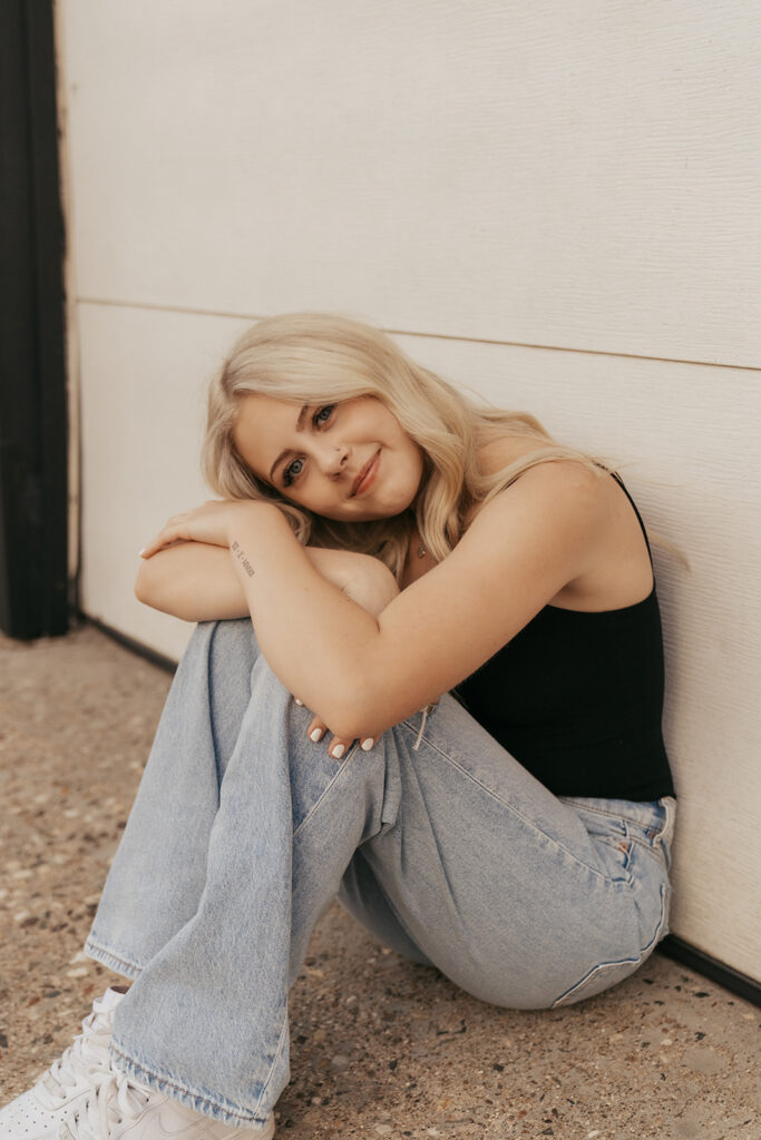 Girl wearing denim light wash jeans lays her head on her knees
