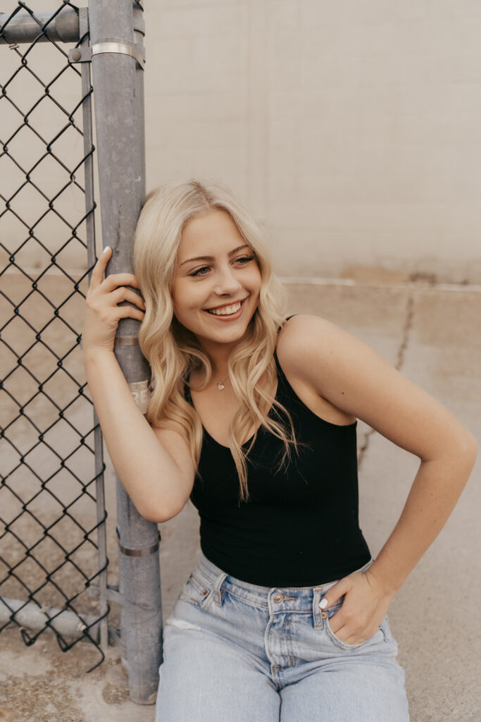 Senior photos Minneapolis where girl leans against fence in urban setting of St. Anthony Main