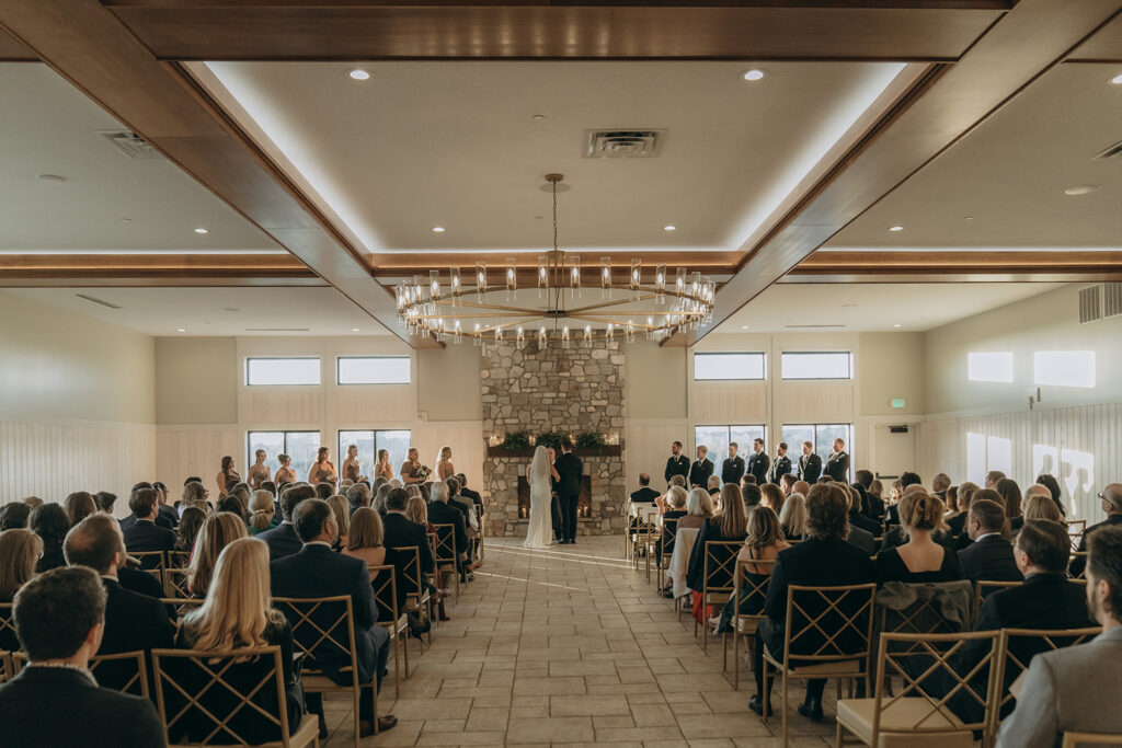 Wide ceremony shot of the couple exchanging vows at Equestria West in Chaska, Minnesota — a November wedding with soft candlelight and stone fireplace warmth.