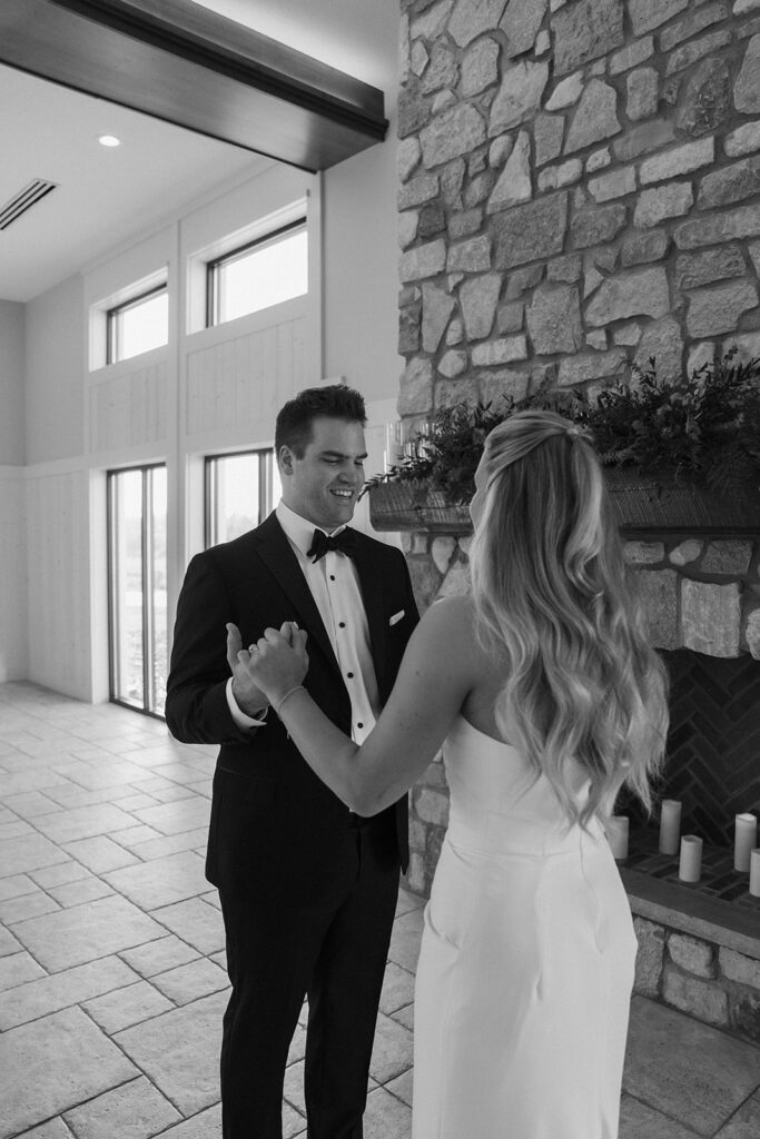 Black and white image of the couple holding hands before the ceremony, standing near a fireplace adorned with candles in Chaska.