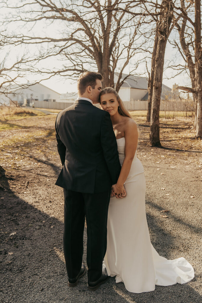 Bride and groom holding hands beneath bare November trees in Chaska, Minnesota, pausing for a quiet portrait before their candlelit wedding ceremony.