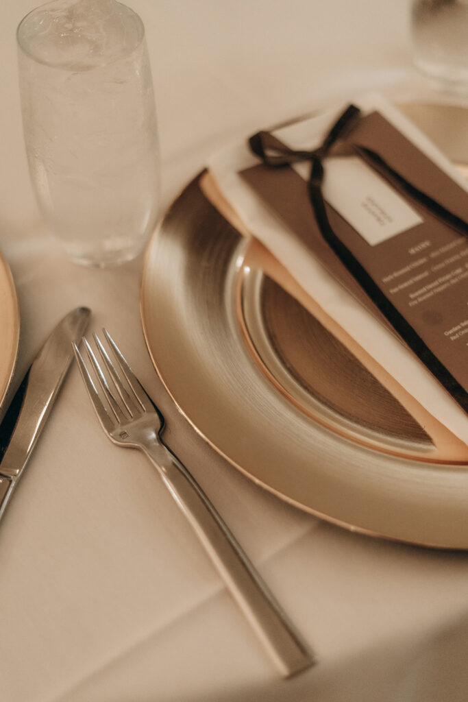 A detail shot of the elegant place setting with a chocolate brown menu card and satin ribbon on a gold charger