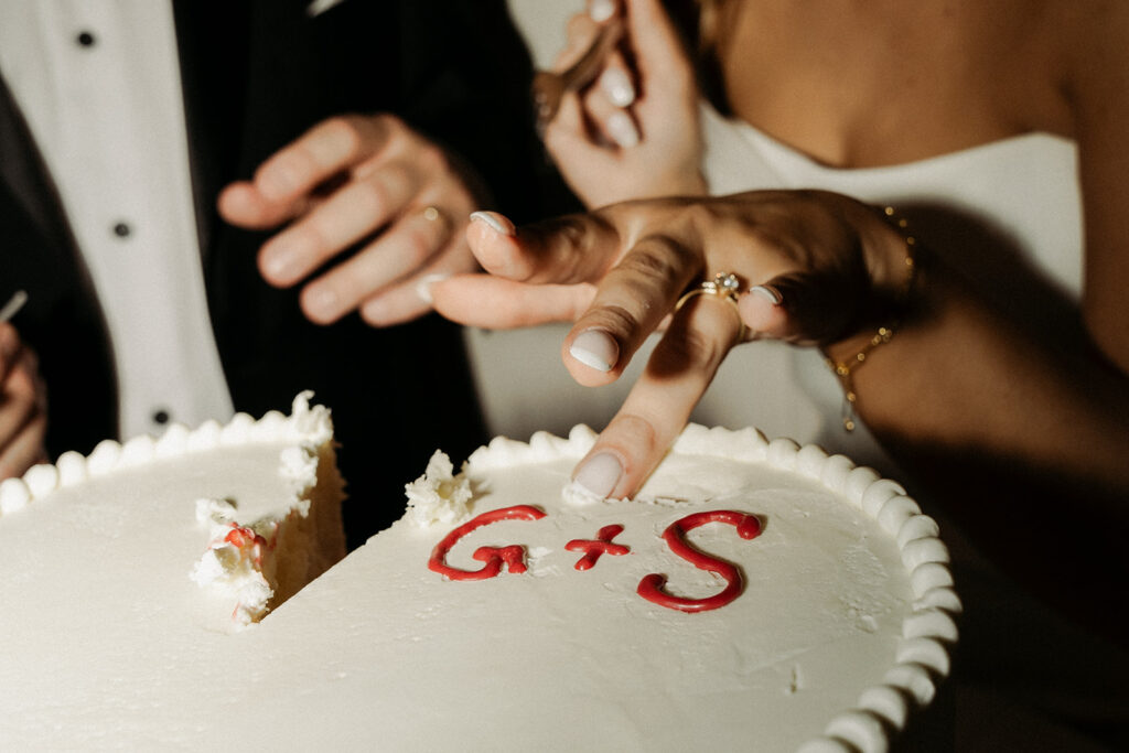 Close-up of the couple cutting into their wedding cake marked with “G + S” during their November reception in Minnesota.