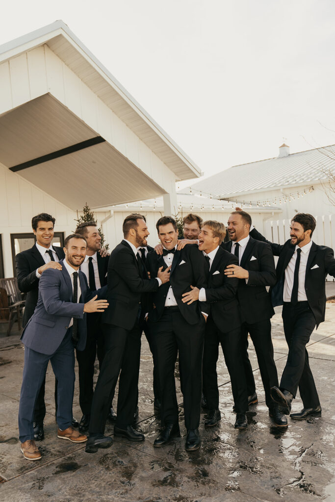 The groom laughing with his groomsmen during portraits outside Equestria West at their Chaska wedding venue.
