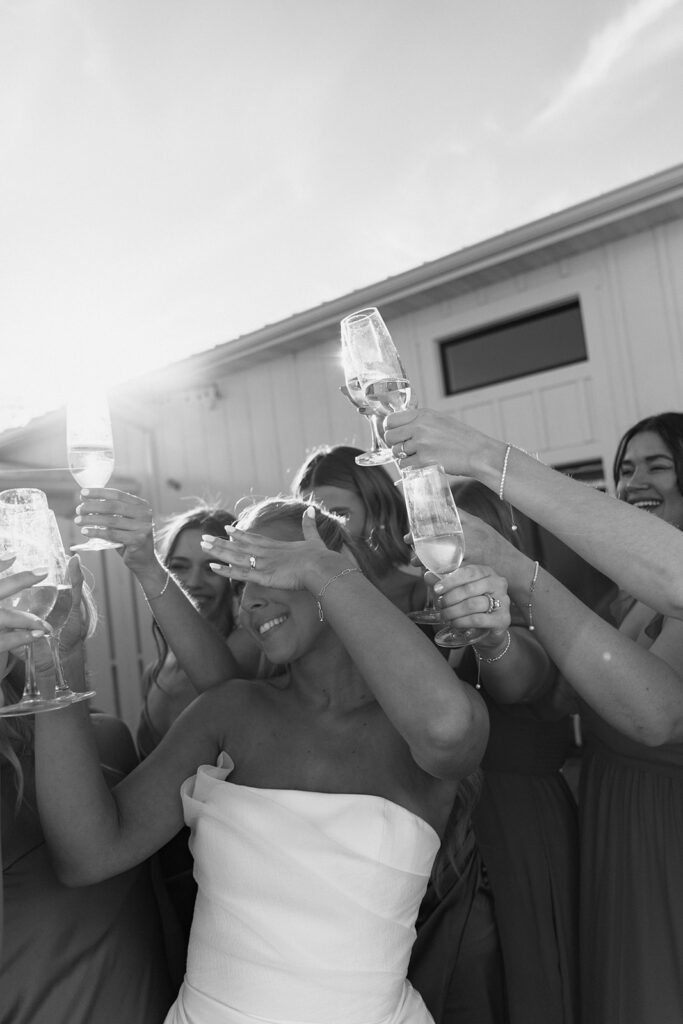 The bride smiling through a champagne toast with her bridesmaids on the morning of her candlelit fall wedding.