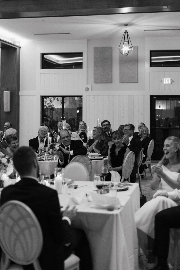 Wedding guests laugh during toasts at a warmly lit fall reception in Chaska, Minnesota.
