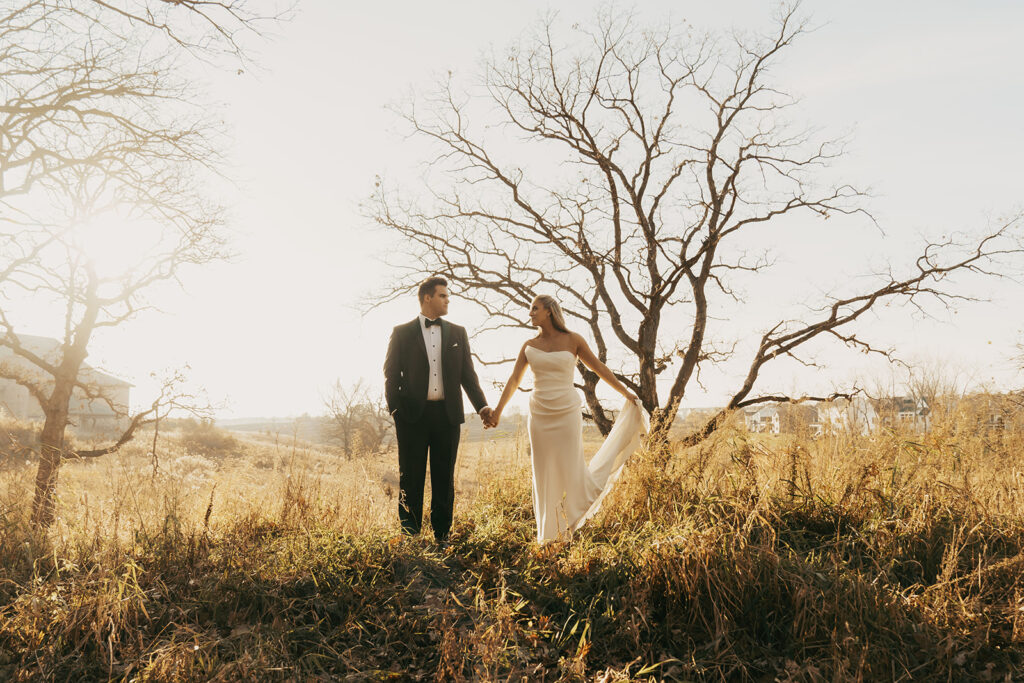 Bride and groom walking hand-in-hand through golden November fields in Chaska, Minnesota — a soft, romantic start to their candlelit wedding day.