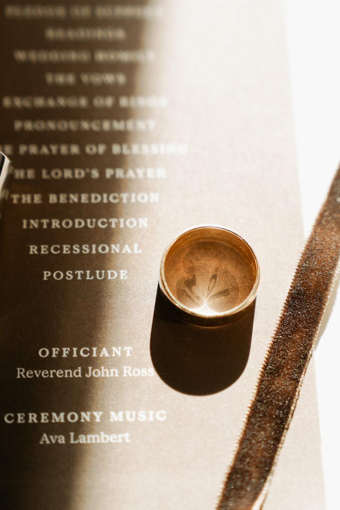 Gold wedding ring resting on the printed ceremony program, catching warm November sunlight in Chaska.