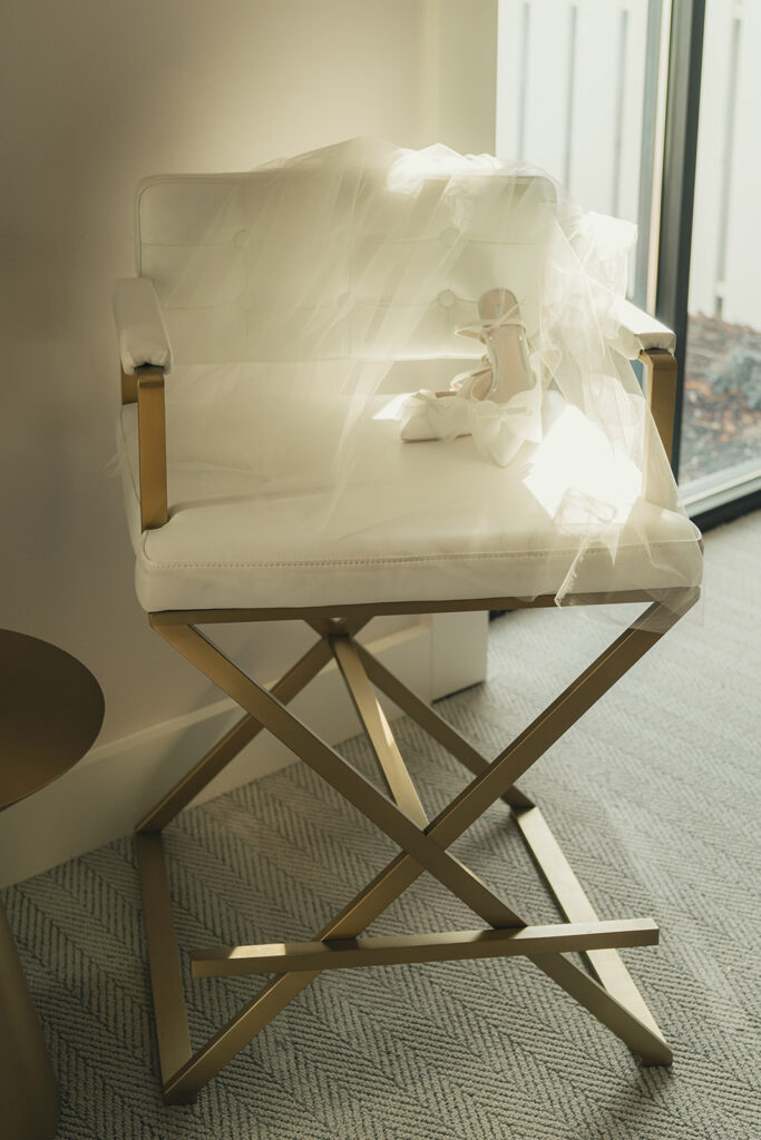 Her veil and shoes arranged on a gold chair near the window, softly lit by late autumn sun.