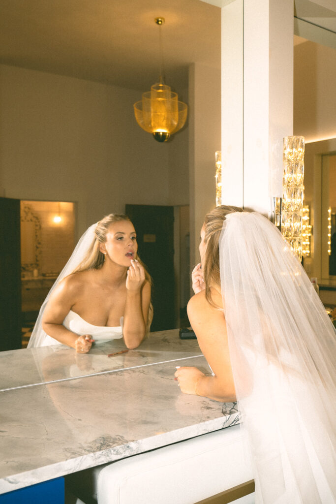 The bride applying lipstick in front of a marble vanity, getting ready for her candlelit November wedding in Chaska.
