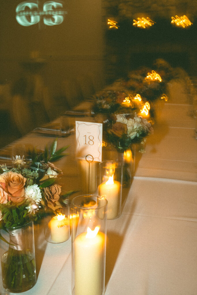 A glowing, slightly motion-blurred image of a floral and candle-lined reception table with table number 18