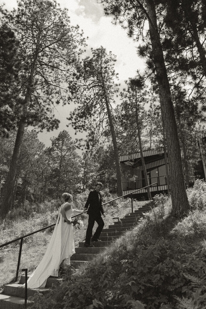 Groom leads bride up staircase towards Catalyst by Nature Link wedding venue in Minnesota