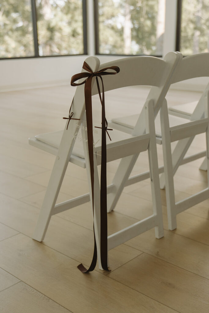 White chairs with simple espresso colored bows tied on the corners