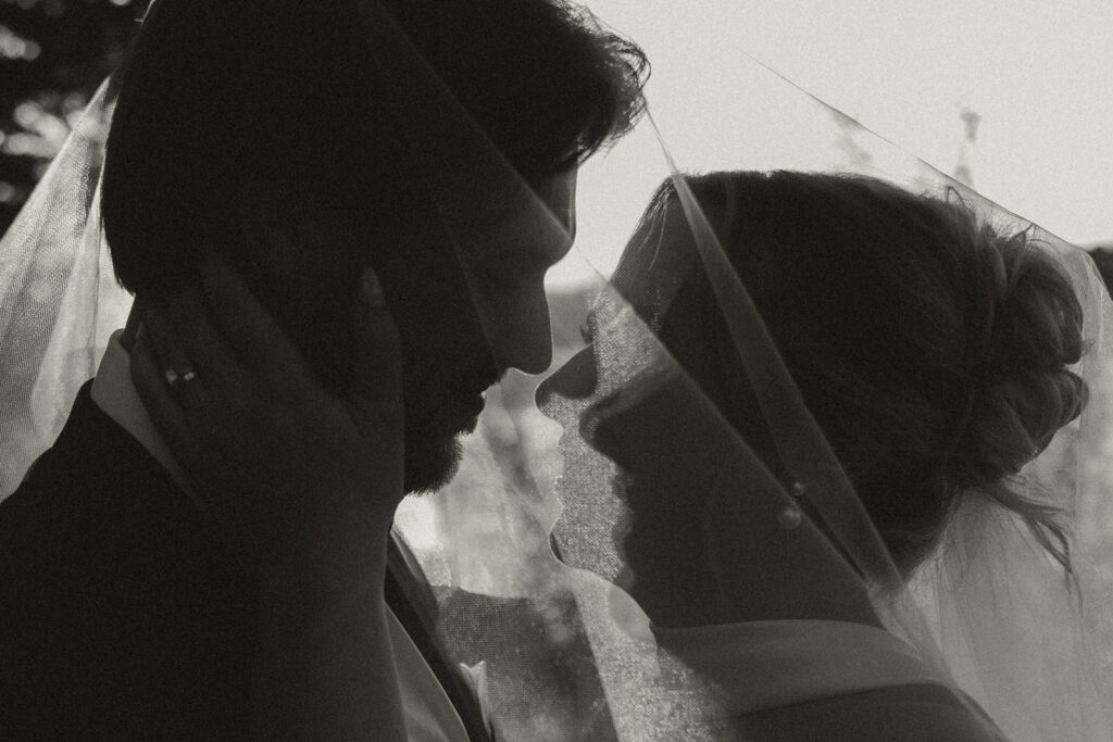 Bride cradles groom's face as he leans in for a kiss under the cover of her veil