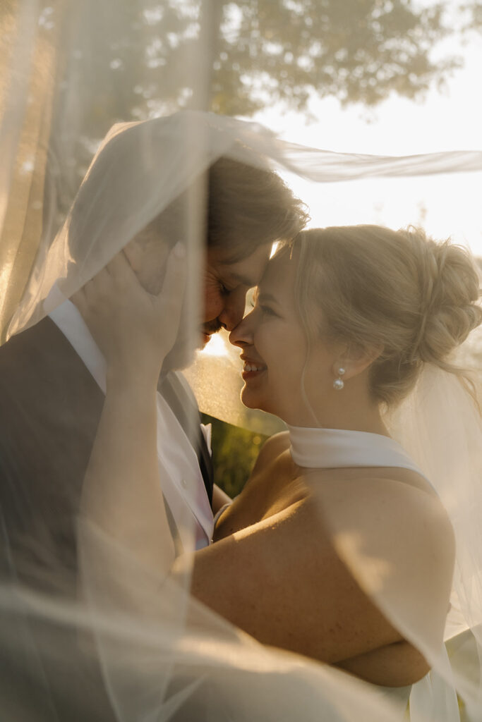 Bride and groom touch noses under bride's cathedral veil for timeless wedding photos