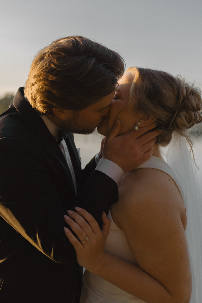 Groom kisses bride while cradling her neck during blue hour timeless wedding photos