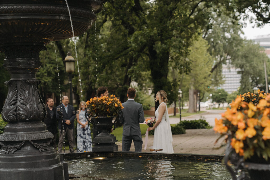 Couple stands at the fountain surrounded by family during their Irvine Park wedding ceremony.