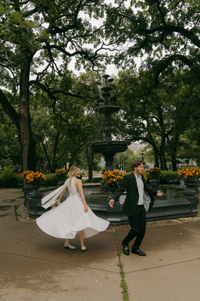 Bride and groom frolicking together by the gothic fountain in Saint Paul’s Irvine Park.