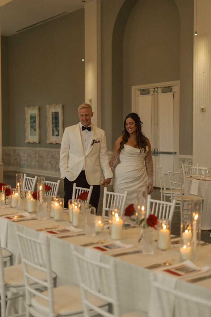 Bride and groom walking hand in hand past candlelit tables at their elegant St. Paul wedding.