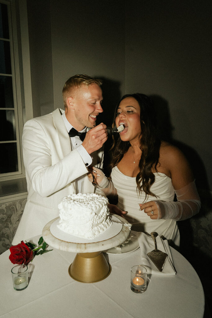 Groom feeding bride cake at their classy black-tie wedding reception in Minnesota.