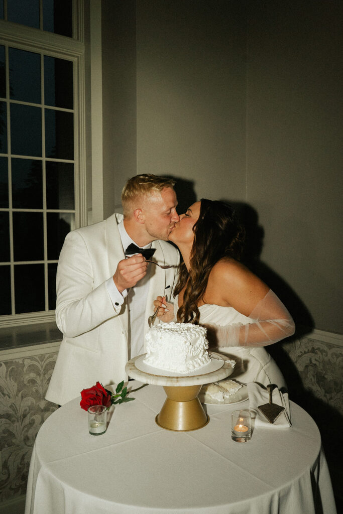 Bride and groom sharing a kiss over their timeless white wedding cake in Minnesota.