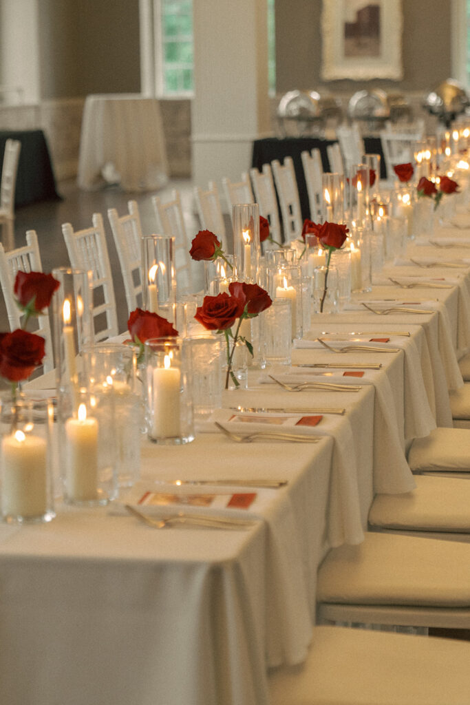 Long harvest table lined with red roses and candles at a classic Minnesota wedding reception.