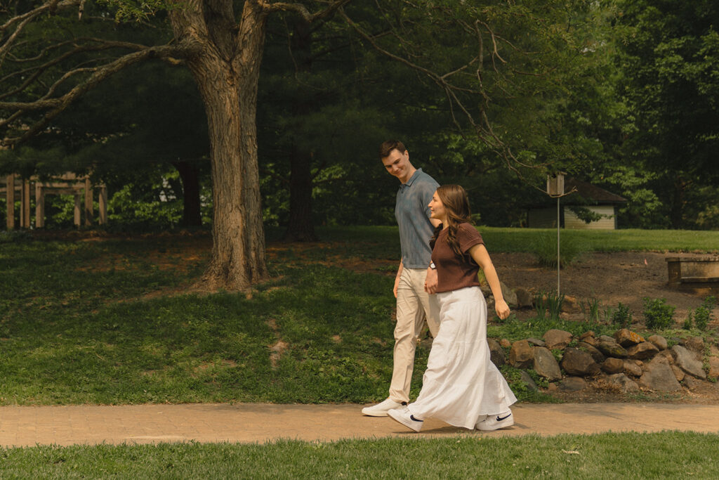 Joey and Bella walking together along a shaded path at Noerenberg Gardens, smiling and relaxed after the proposal.
