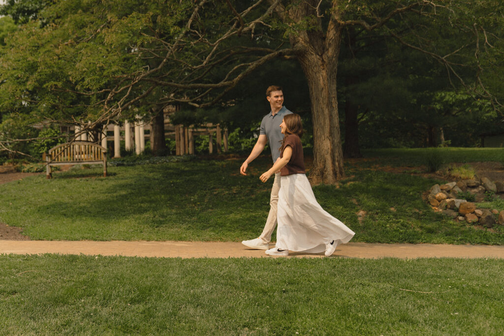 Joey and Bella walking together along a shaded path at Noerenberg Gardens, smiling and relaxed after the proposal.