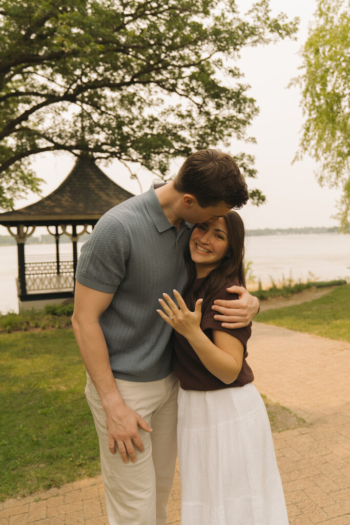 Bella leaning into Joey as they stand near the gazebo, smiling after their engagement at Noerenberg Gardens.