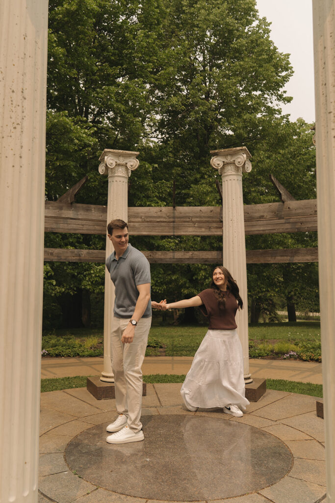 Joey and Bella laughing as they walk between the stone columns at Noerenberg Gardens, captured by wedding proposal photographer.