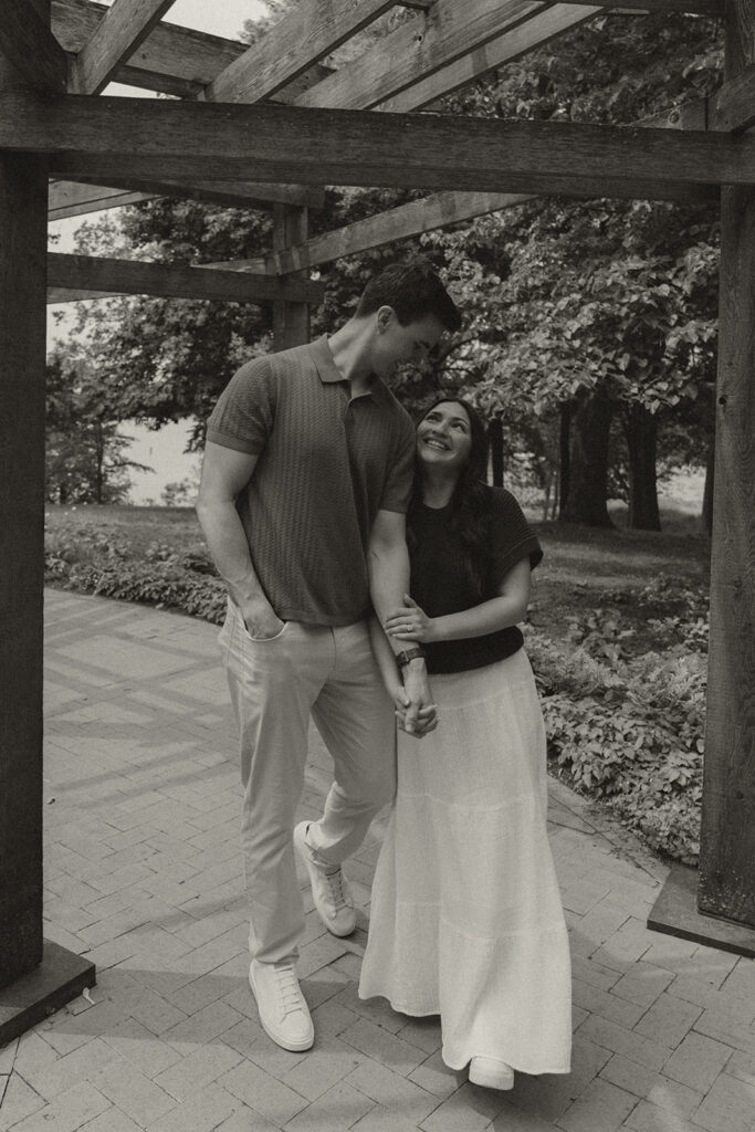 Wedding proposal photographer captures Joey looking down at Bella while they stand together beneath the wooden pergola.