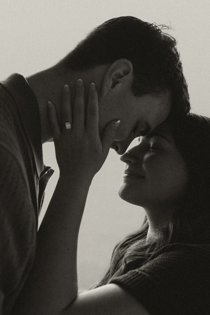 Close-up of Joey holding Bella’s face as she smiles, her engagement ring visible against his cheek.