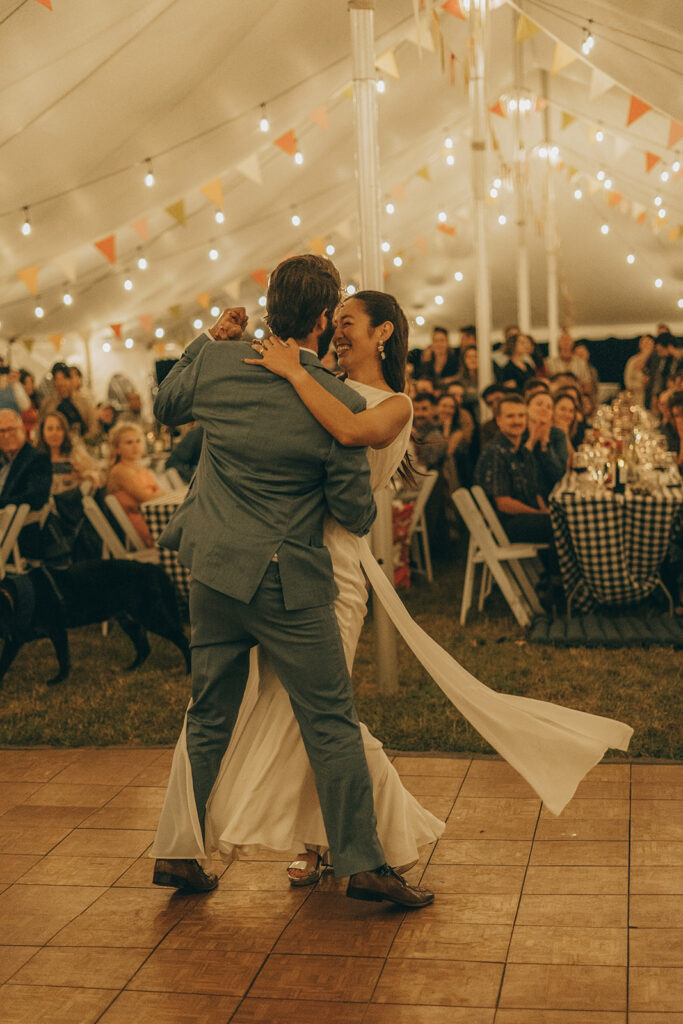 Eura and Stu sharing a slow dance on the wooden dance floor under string lights, surrounded by family and friends at their backyard wedding.