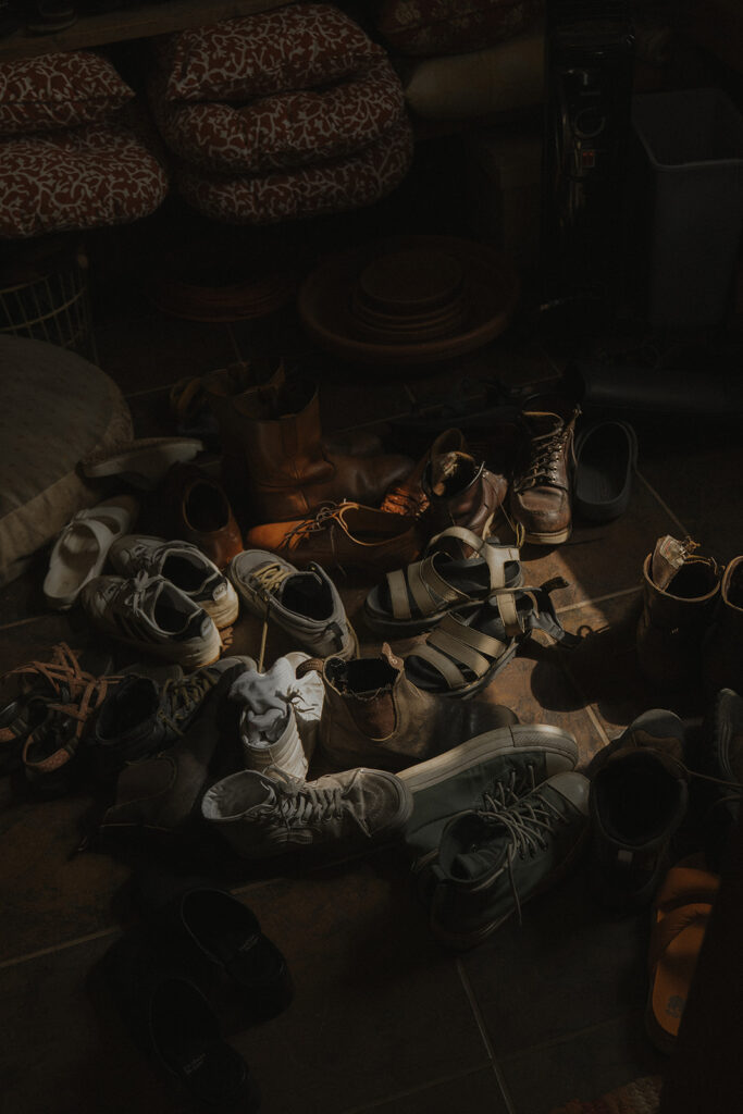 A growing pile of guests’ shoes in the farmhouse entryway during the getting ready portion of this backyard wedding, a sign of a full house and a full heart.