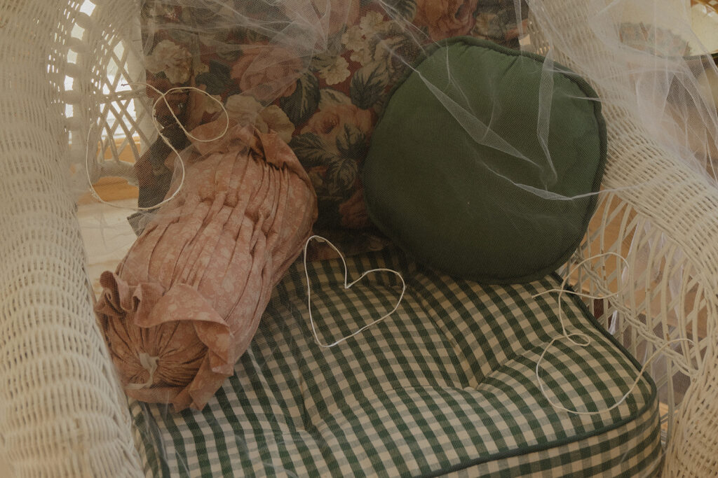 Eura’s wedding veil resting on a wicker chair with floral and gingham cushions, a quiet detail from her garden wedding party morning.