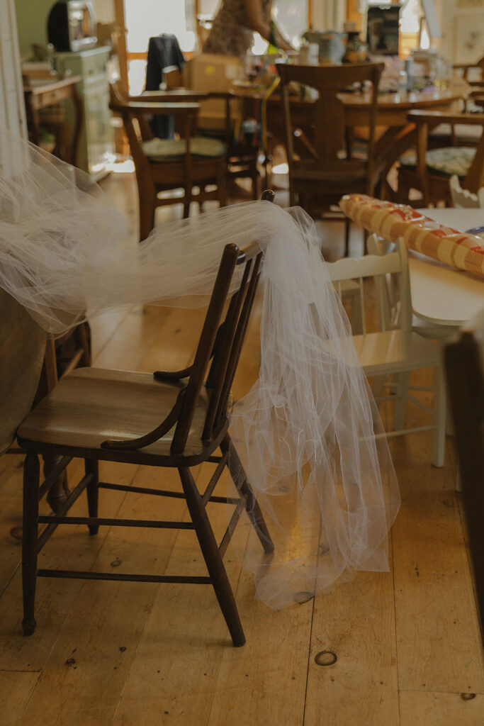 Eura’s embroidered veil draped over a wooden chair in the sunroom of the farmhouse — a quiet, lived-in detail showing the charm of getting ready at home for a backyard wedding.