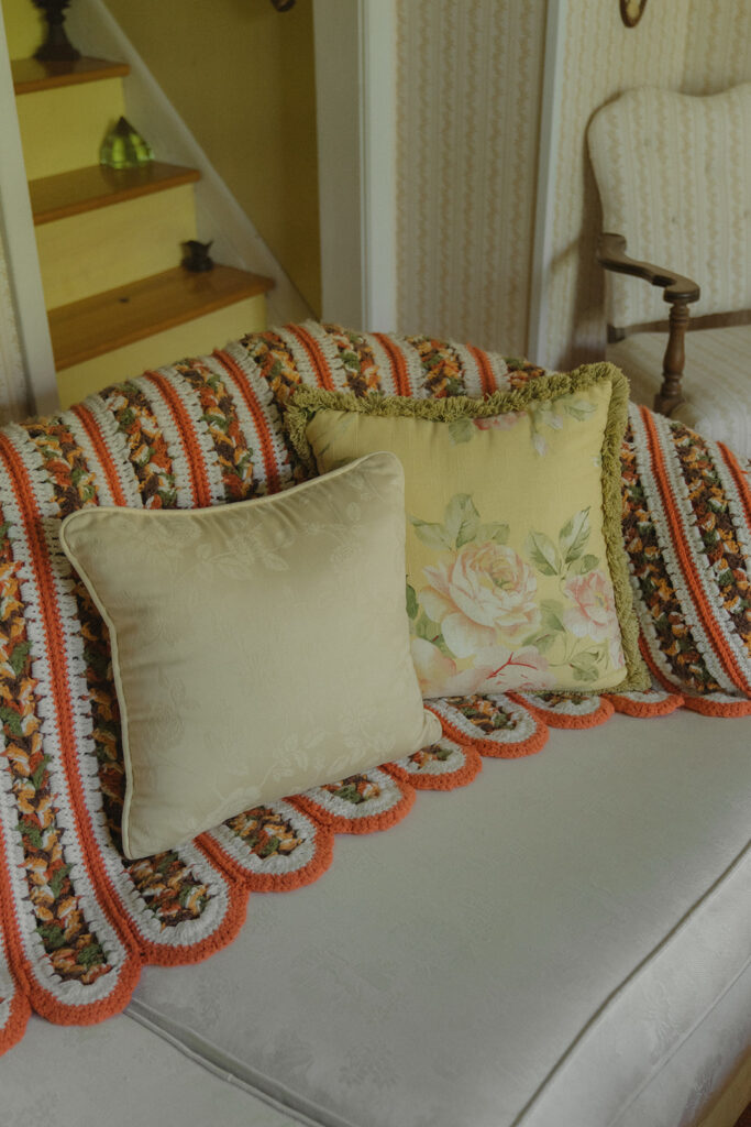 A vintage floral couch layered with a crocheted blanket and pillows inside the farmhouse, capturing the cozy atmosphere of this at-home garden wedding party.