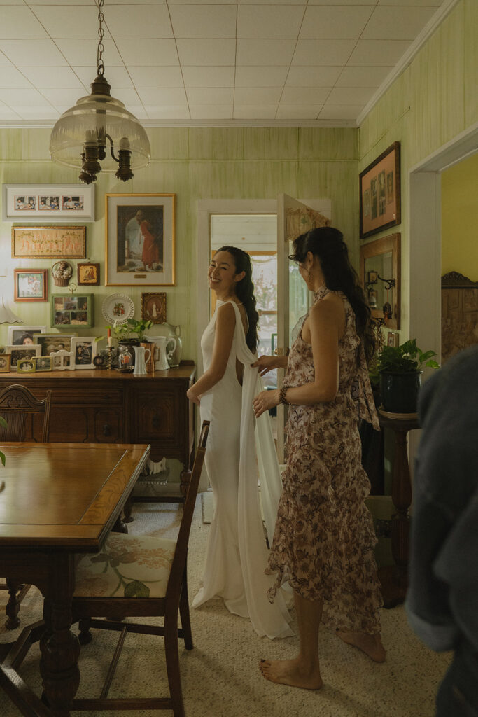 Eura walking through the farmhouse living room with a friend nearby, surrounded by heirlooms and family photos that shaped the story of this backyard wedding.