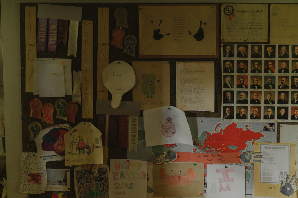 A bulletin board covered in ribbons, certificates, and childhood drawings inside the farmhouse, showing the layered history behind this sentimental backyard wedding venue.