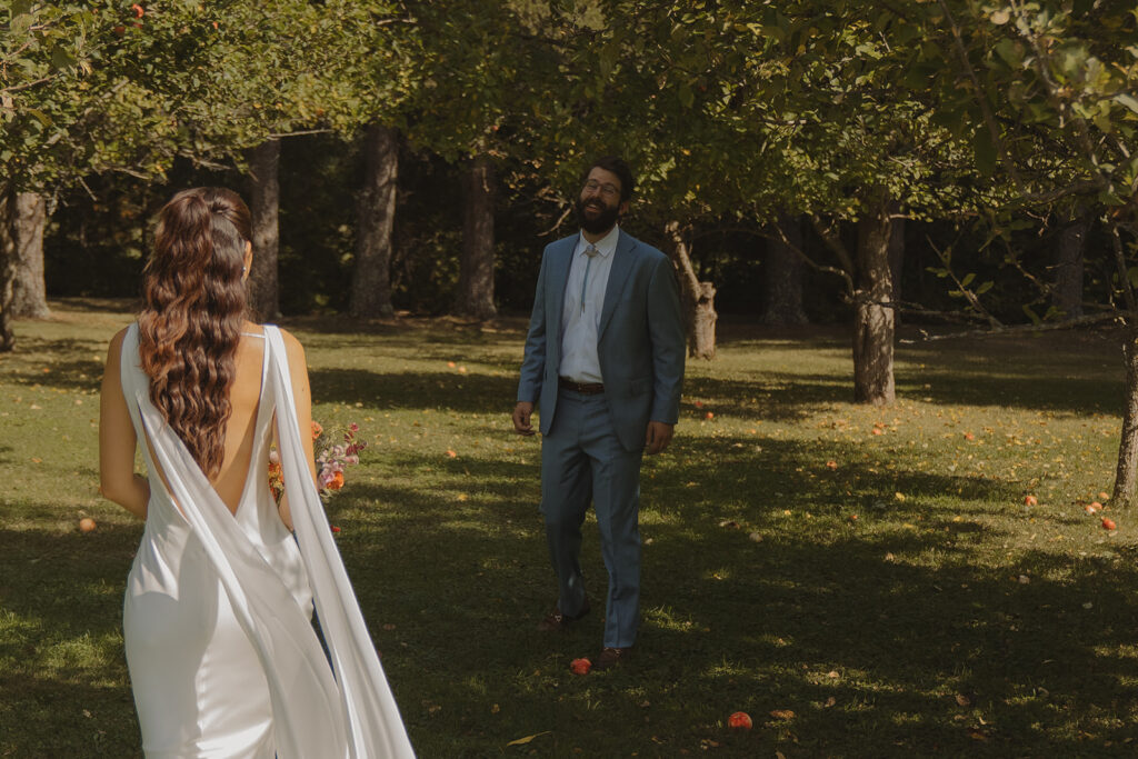 Eura walking toward Stu for their first look in the orchard, a simple and heartfelt backyard wedding idea surrounded by trees.